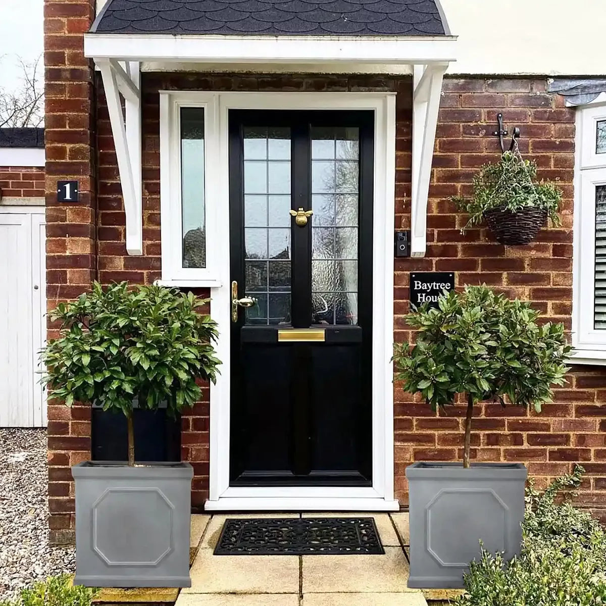 A brick house’s front door gets an affordable garden decor update with the IDEALIST Lite Chelsea Flower Box Square Garden Planter, a frost-resistant 91L grey pot (W45 H45 L45 cm) featuring pre-drilled drainage holes for easy plant care.