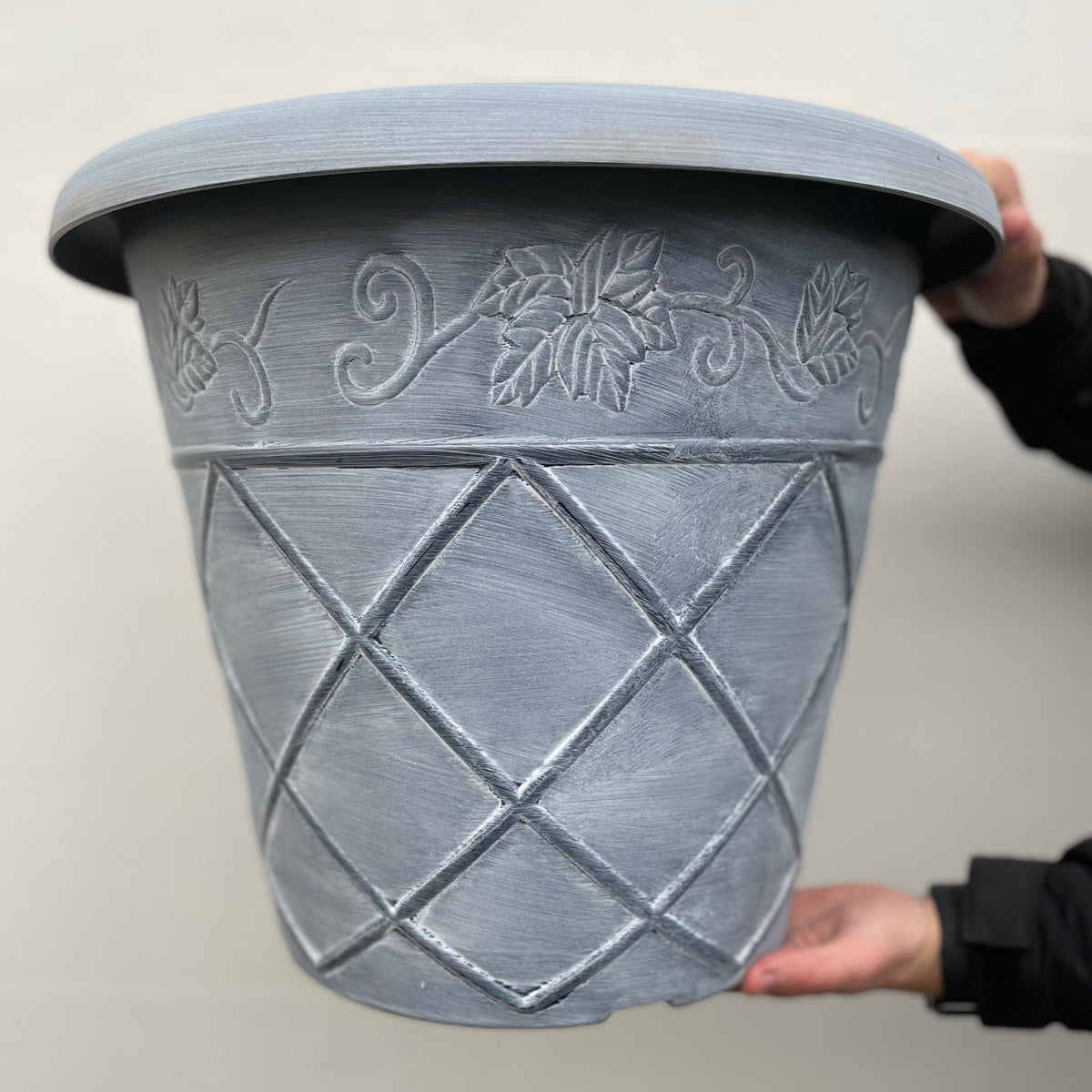 A person holds the Shabby Chic Washed Planter in light blue, featuring a vine and leaf rim and a crisscross diamond body design, against a light background.