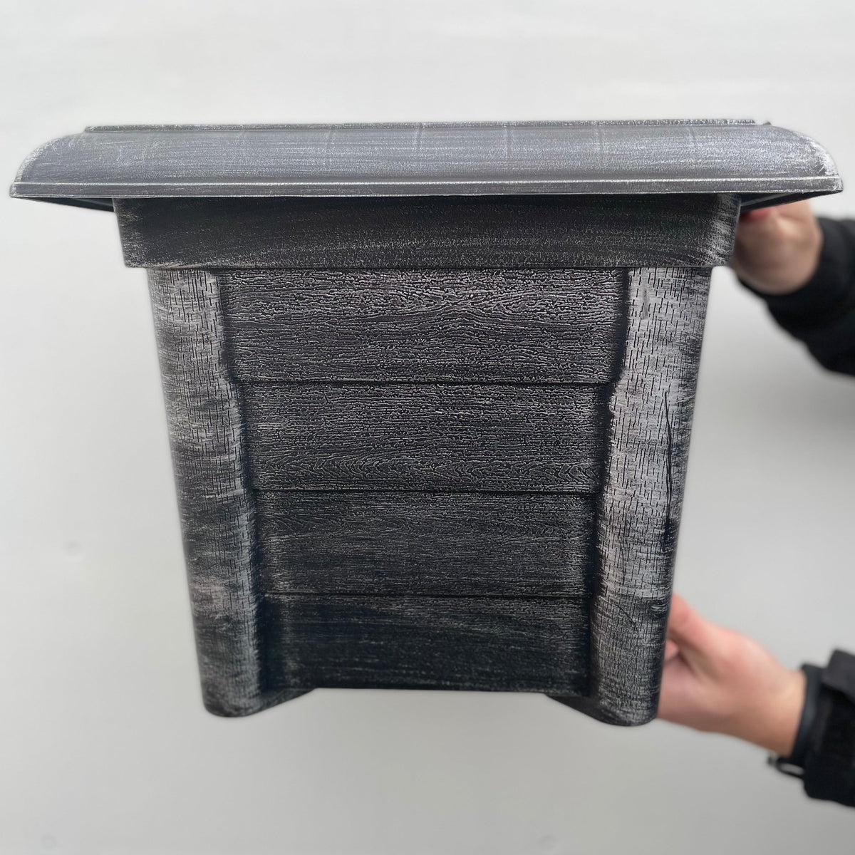 A person holds a Silver Square Planter with drainage holes; its rectangular shape and slanted roof give it a birdhouse-like appearance, set against a plain light-colored background.
