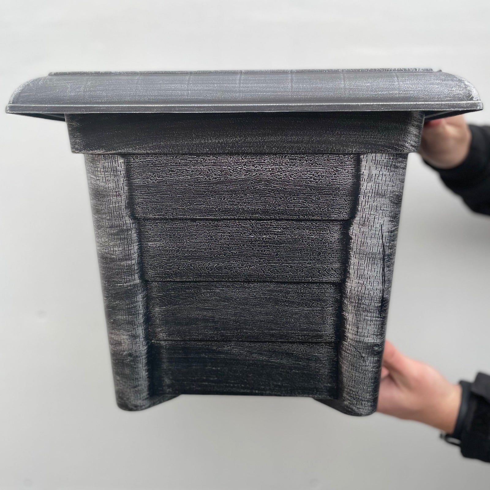 A person holds a Silver Square Planter with drainage holes; its rectangular shape and slanted roof give it a birdhouse-like appearance, set against a plain light-colored background.